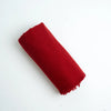 A rolled red fabric cashmere scarf or throw with fringed edges, photographed on a plain white background.