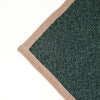 Close-up of a dark green textured blanket corner with a beige ribbed border on a white background.