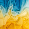 A close-up of draped scarve with a smooth color gradient transitioning from bright yellow at the bottom to pale mint and light blue at the top.